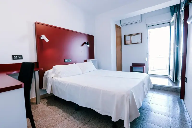 Une chambre lumineuse avec un grand lit blanc et un accès à une terrasse.