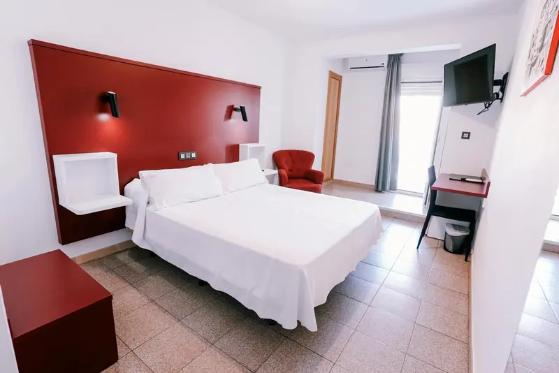 Chambre lumineuse avec un grand lit blanc et un fauteuil rouge.