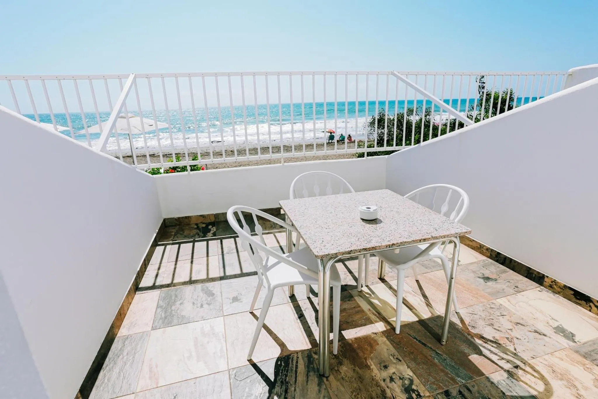Une table et des chaises blanches sur une terrasse carrelée avec vue sur la mer.