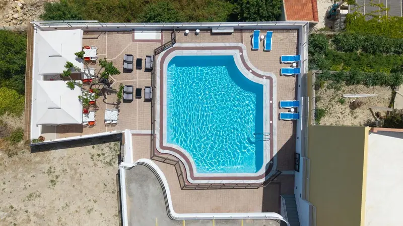 Vue aérienne d'une piscine rectangulaire entourée d'une terrasse avec des transats.
