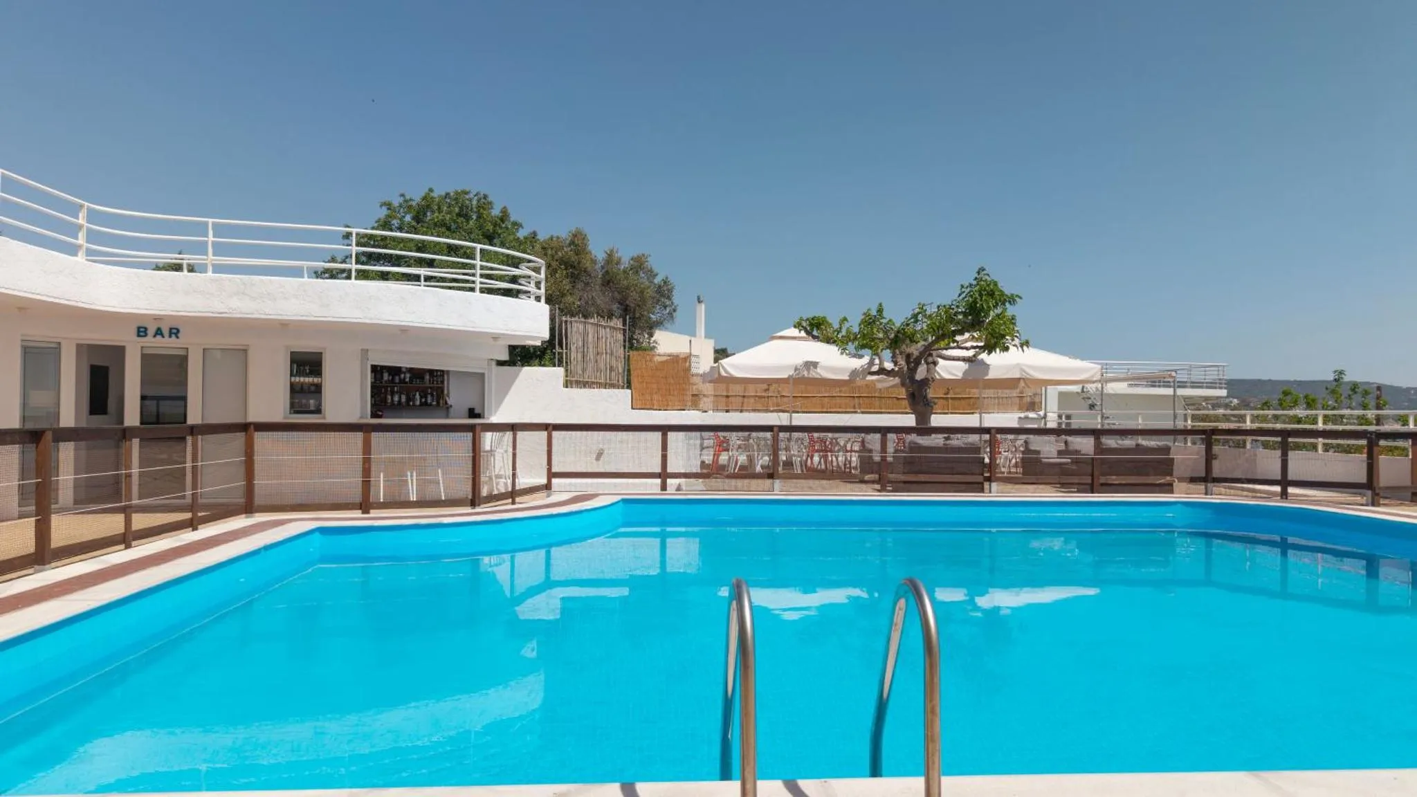 Une piscine bleue bordée d'une terrasse avec un bar et des transats.