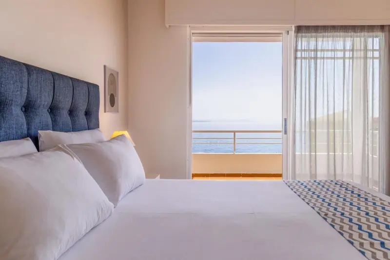Une chambre lumineuse avec un grand lit donnant sur une vue mer.