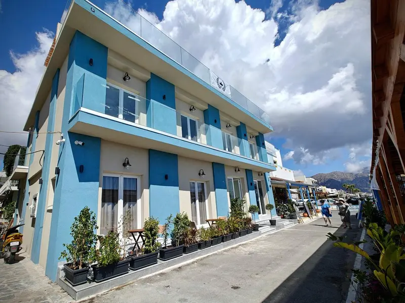 Facade d'un bâtiment bleu à balcons, avec des plantes en pot devant.