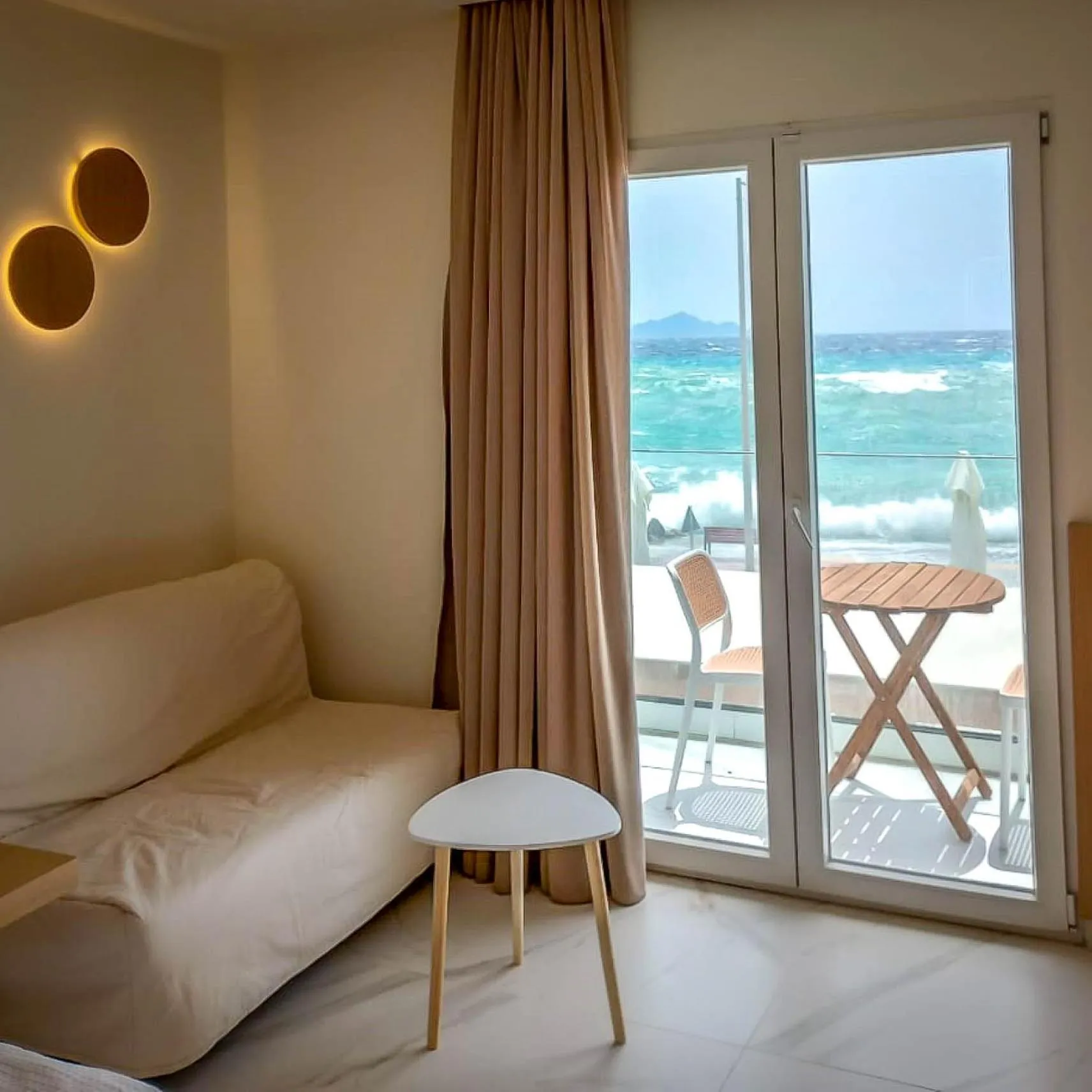 Espace de détente lumineux avec canapé et vue sur la mer depuis un balcon.