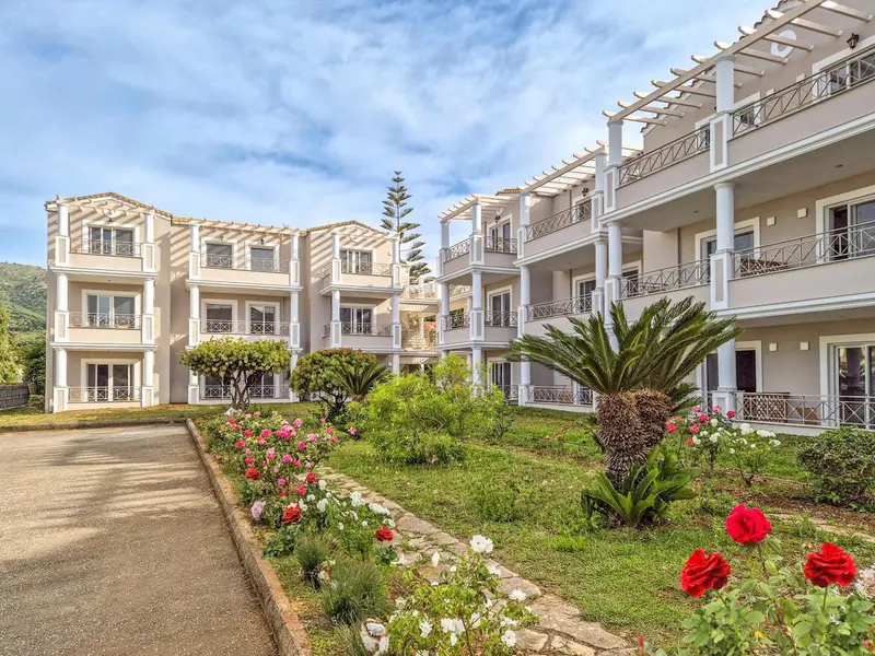 Bâtiment blanc à plusieurs étages avec des balcons et une végétation luxuriante devant.