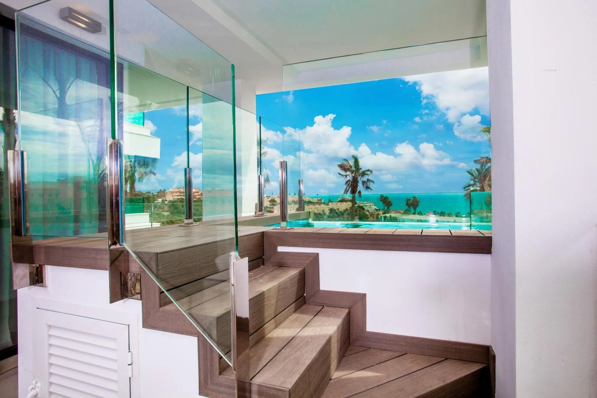 Escalier en bois et verre donnant sur une vue mer et une piscine.