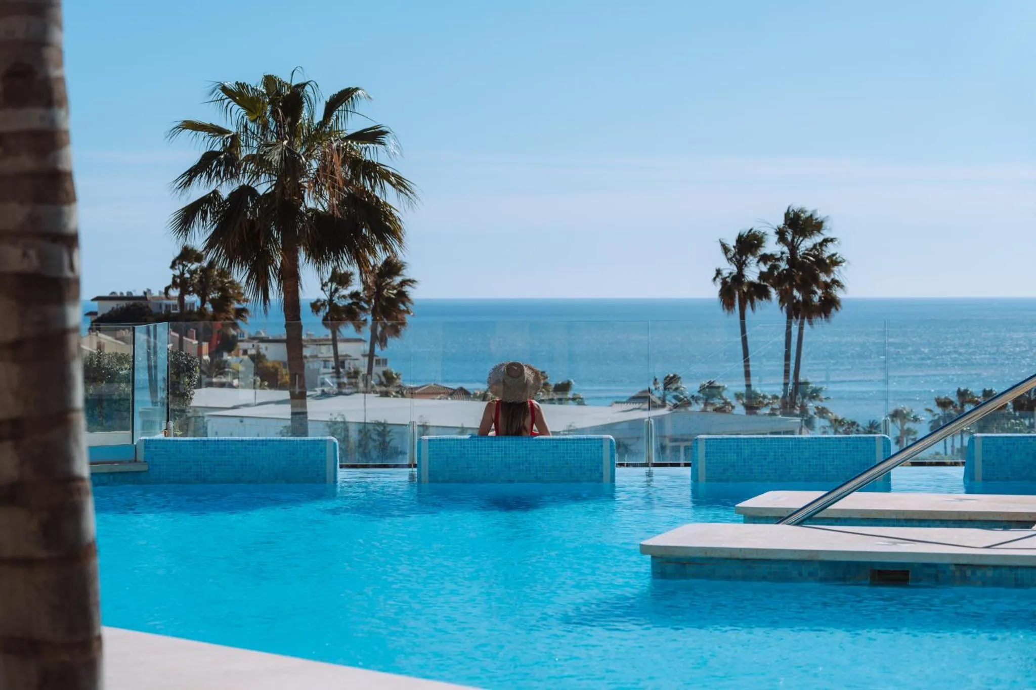 Une personne est assise au bord d'une piscine turquoise avec vue sur la mer.