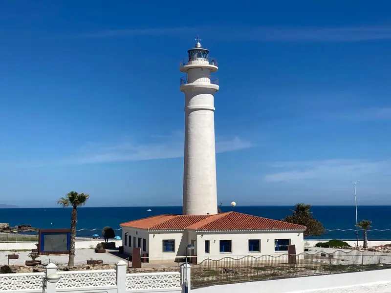 Phare blanc sur une presqu'île rocheuse avec une mer bleue à l'horizon.