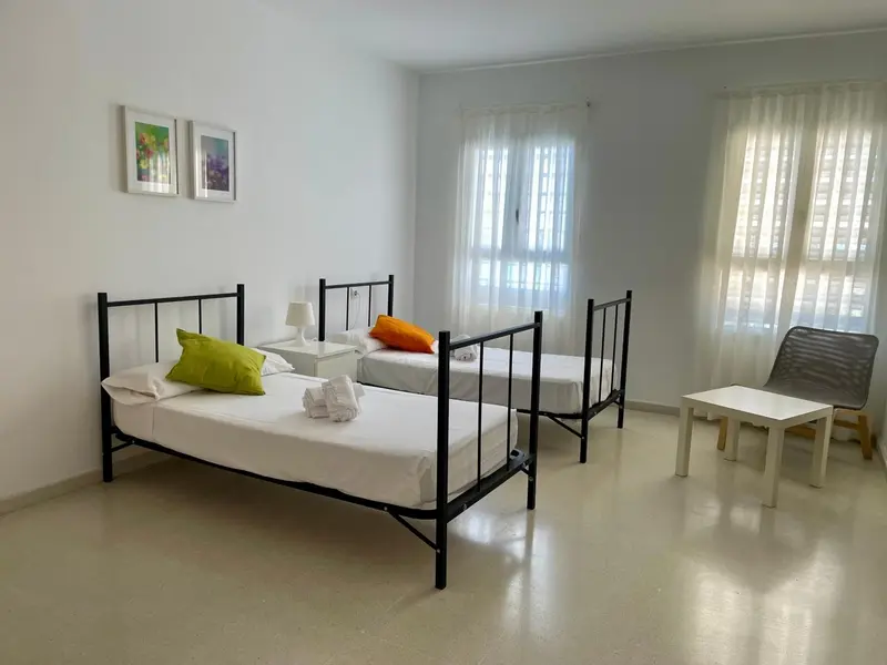 Chambre lumineuse avec trois lits simples et une petite table.