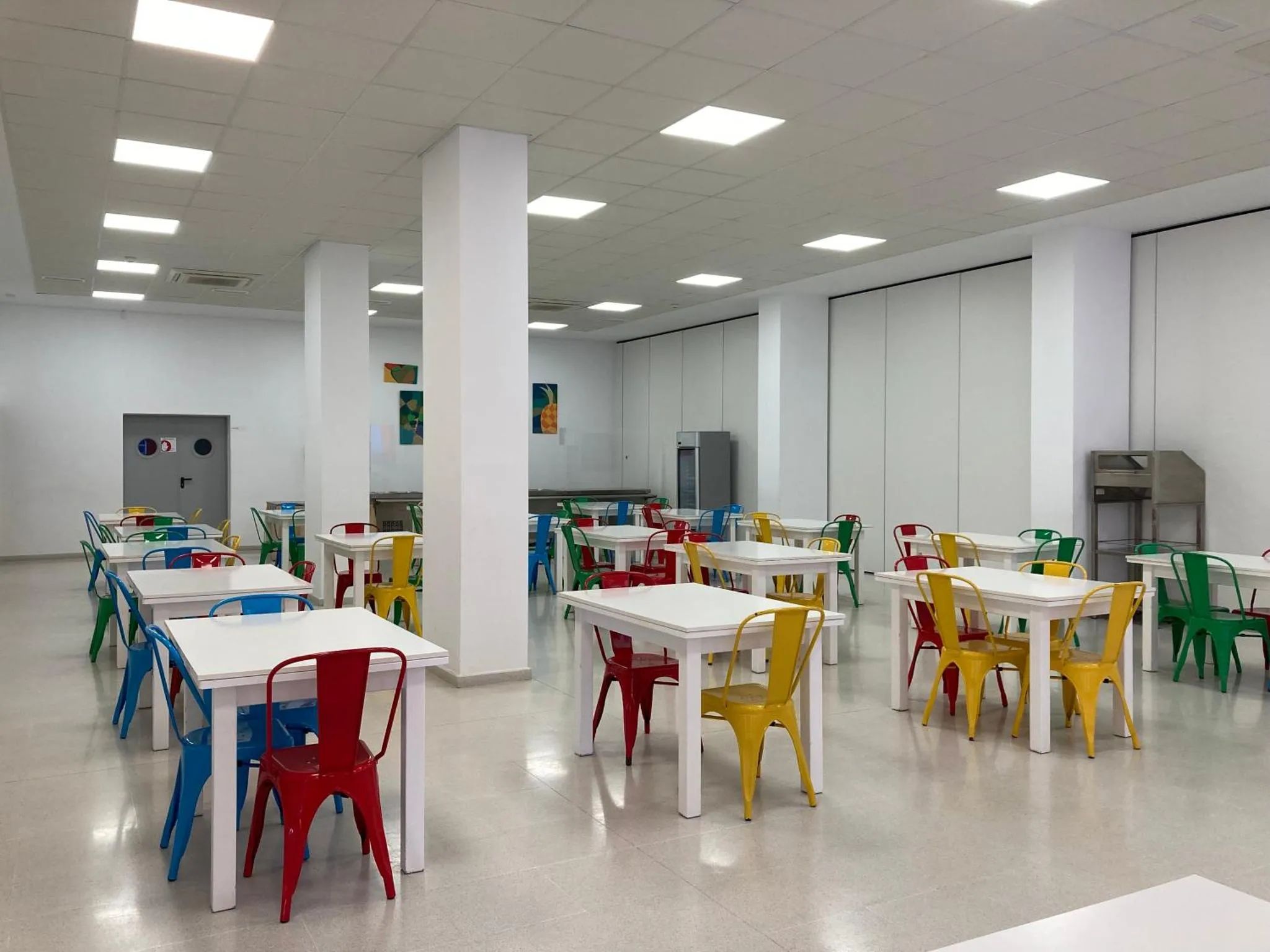 Une salle lumineuse avec des tables et des chaises colorées.