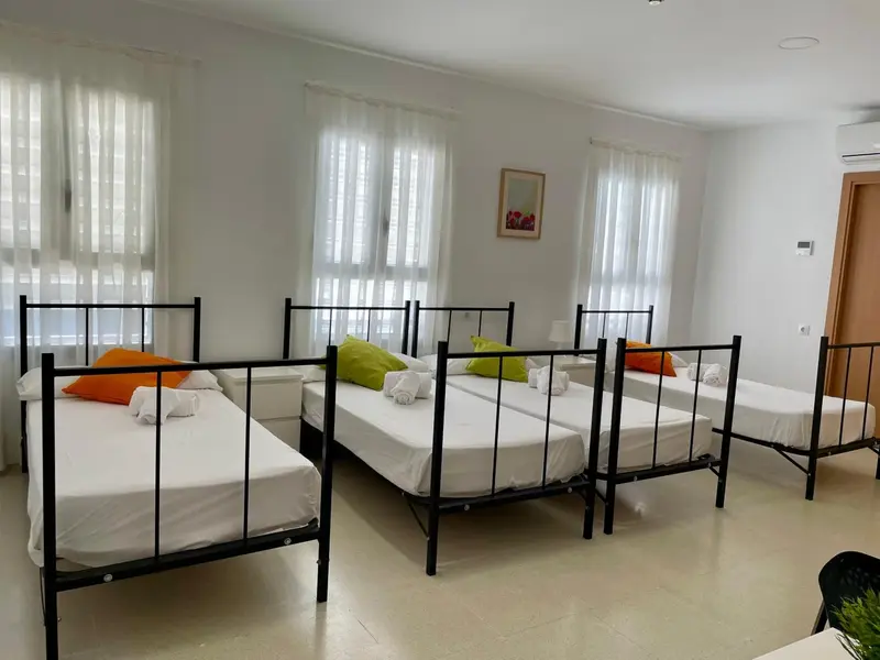Une chambre lumineuse avec plusieurs lits simples et des oreillers colorés.