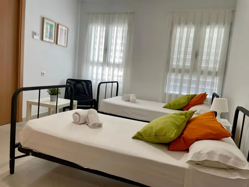 Une chambre lumineuse avec deux lits simples et des oreillers colorés.