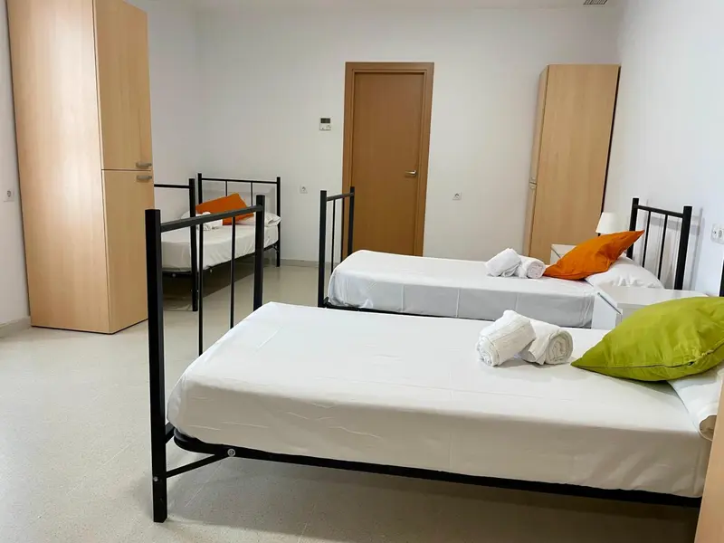 Une chambre lumineuse avec des lits simples et des oreillers colorés.