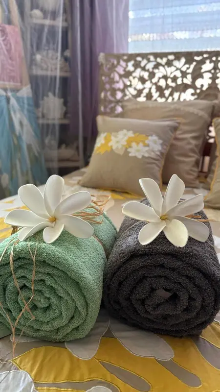 Un lit recouvert d'une courtepointe jaune et de coussins décoratifs, avec des serviettes enroulées et des fleurs.