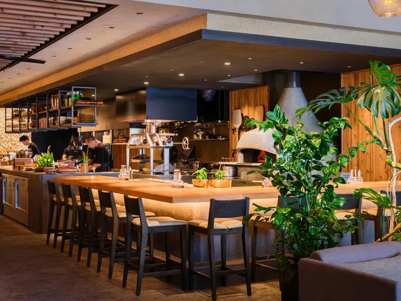 Un comptoir de bar en bois avec des tabourets, éclairé par des suspensions.
