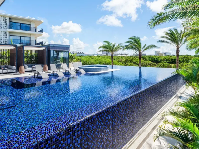 Une piscine à débordement bleu turquoise avec des transats et des palmiers.