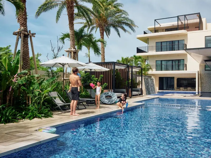 Une piscine bordée de transats et de palmiers devant un bâtiment beige.