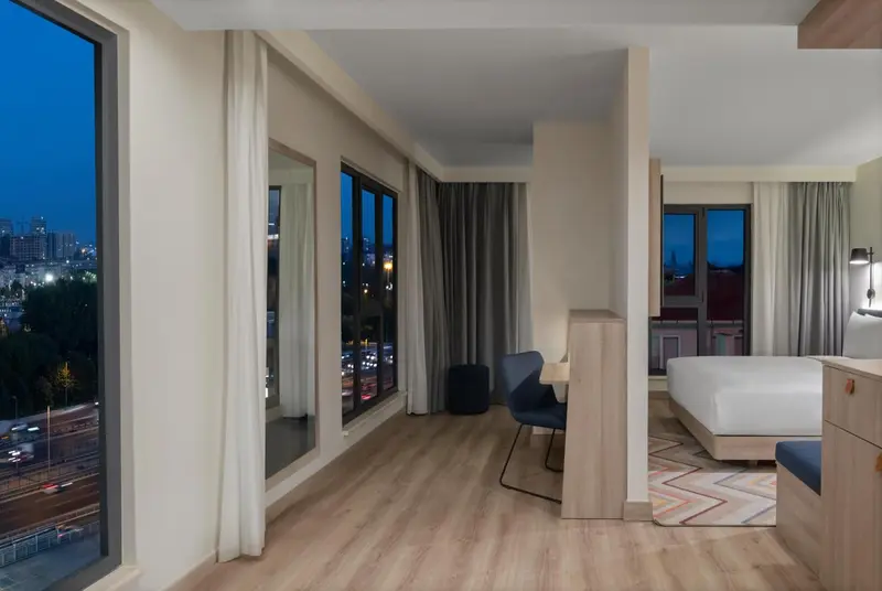 Une chambre lumineuse avec un bureau près d'une grande fenêtre donnant sur la ville.