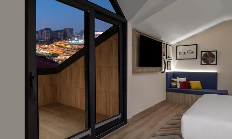 Une chambre moderne avec un grand balcon vitré donnant sur une ville illuminée.