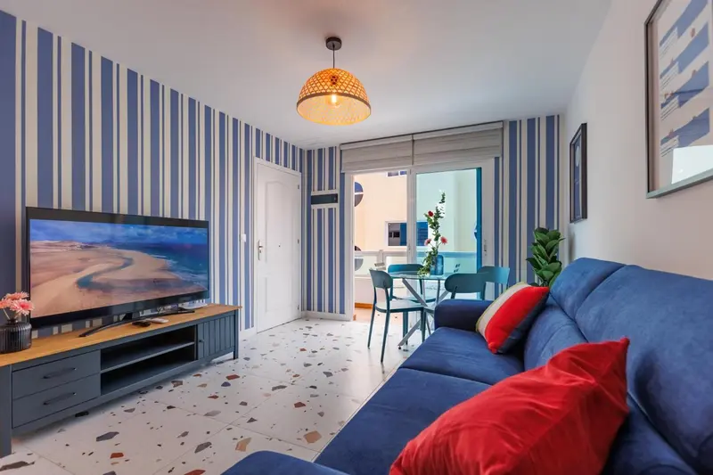 Un salon lumineux avec canapé bleu et télévision face à une table à manger.
