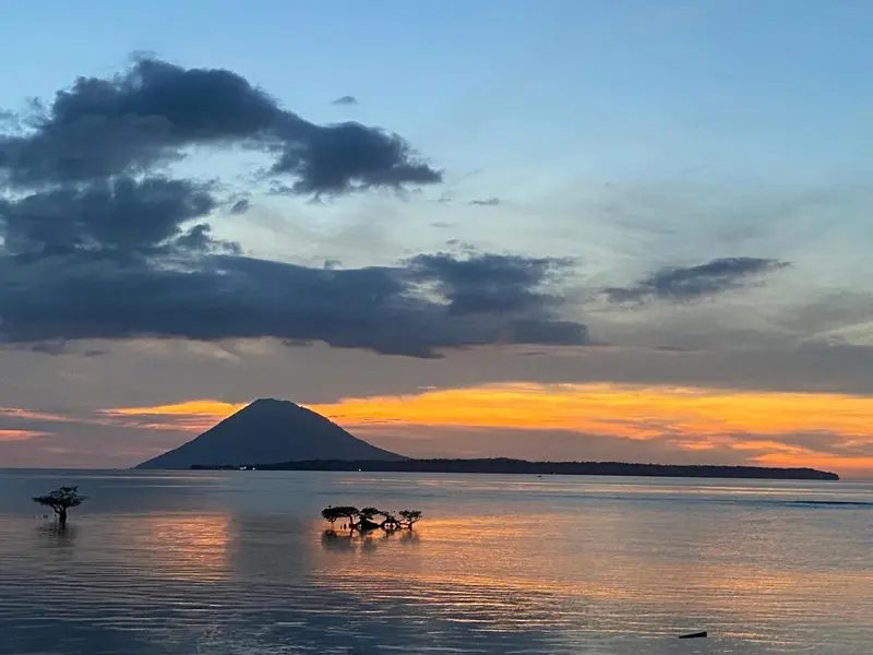 Coucher de soleil sur une mer calme avec une île volcanique en arrière-plan.