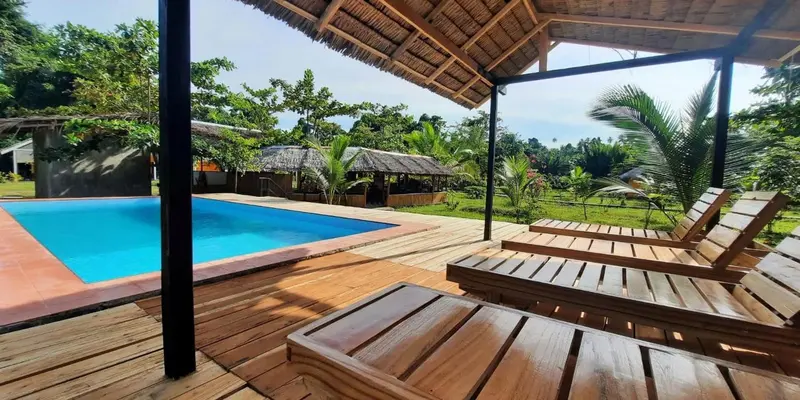 Terrasse en bois avec transats donnant sur une piscine et une végétation tropicale.