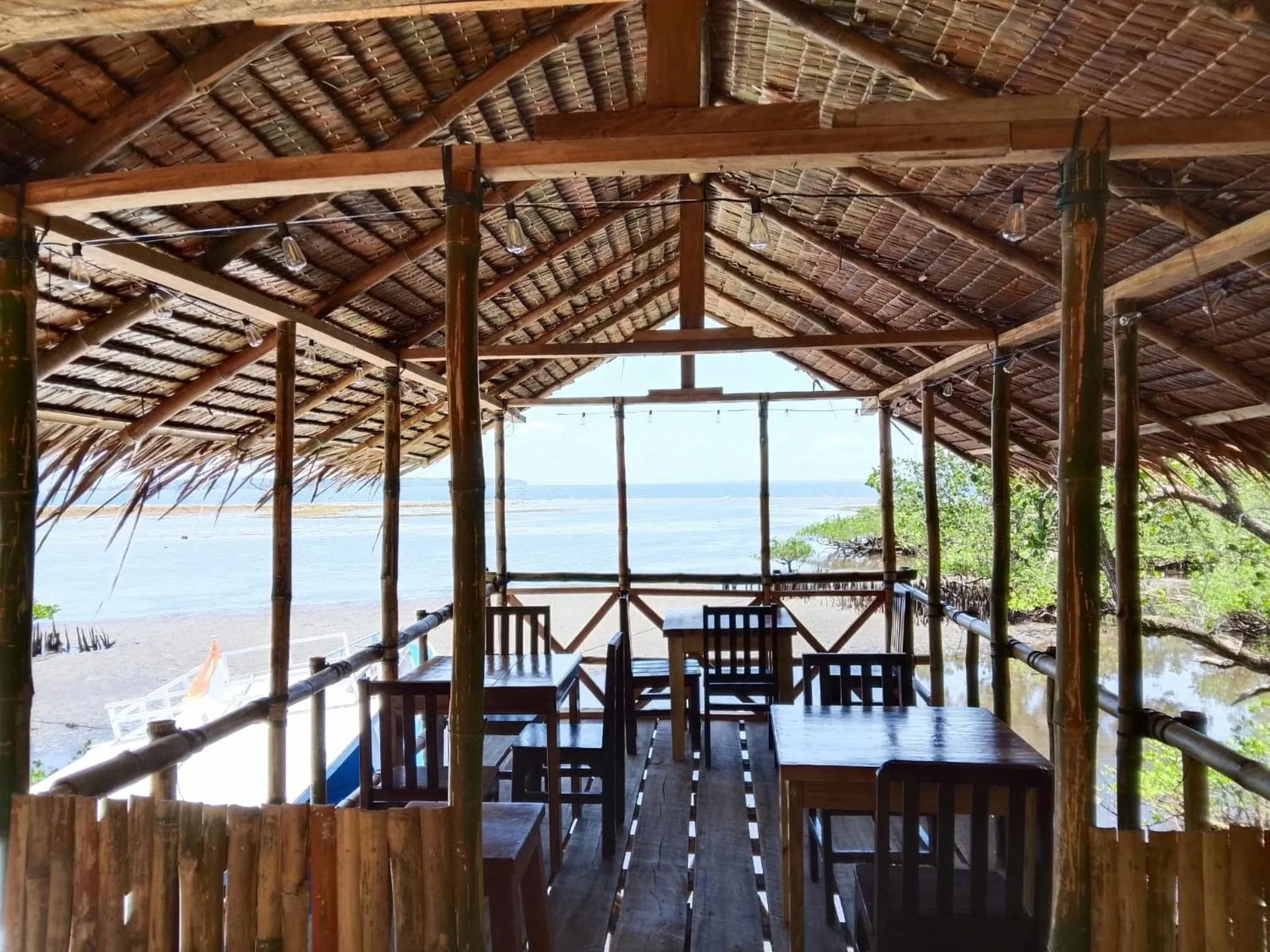 Terrasse ombragée avec tables et chaises donnant sur la mer.