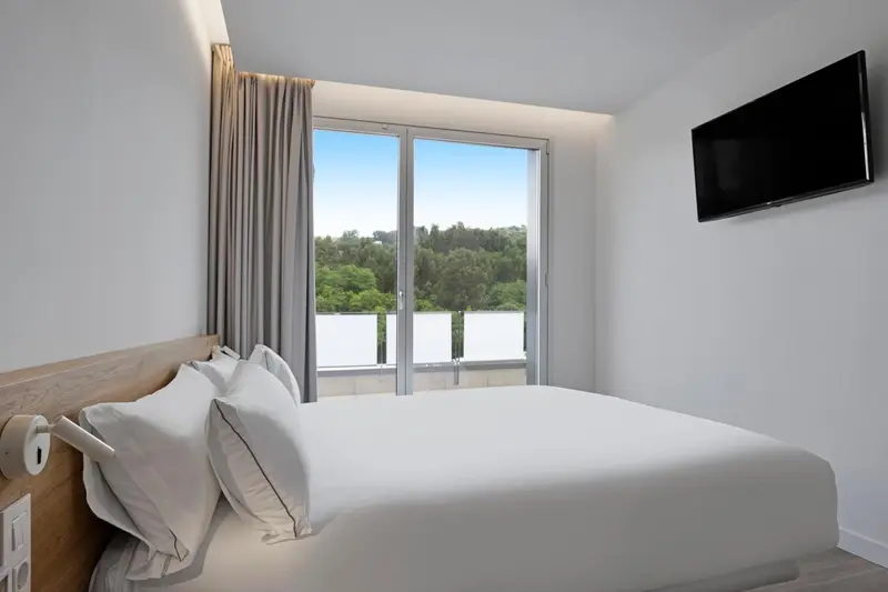 Une chambre lumineuse avec un grand lit et une vue sur la végétation.