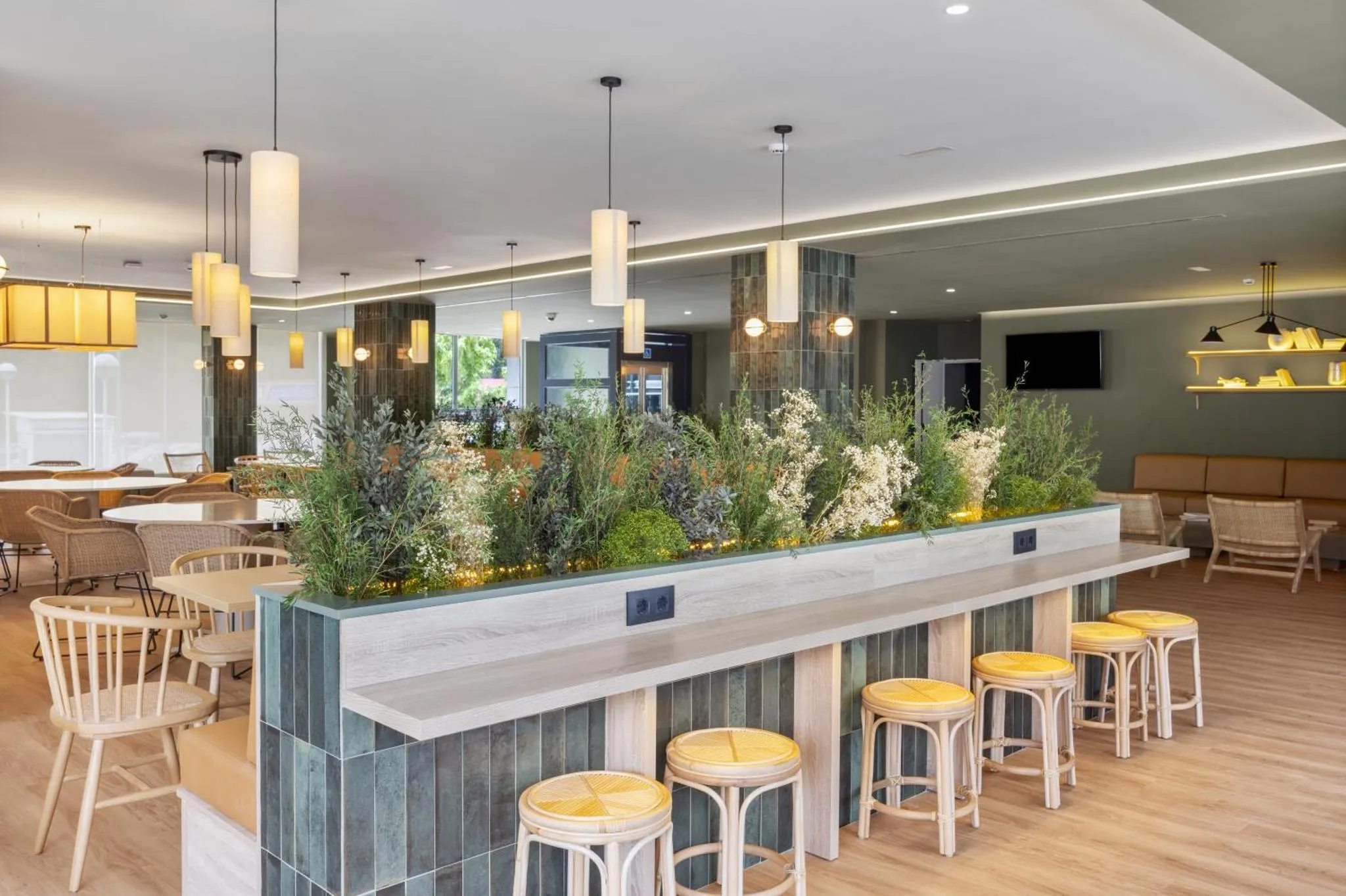 Une salle lumineuse avec des tables, des chaises et un long comptoir végétalisé.