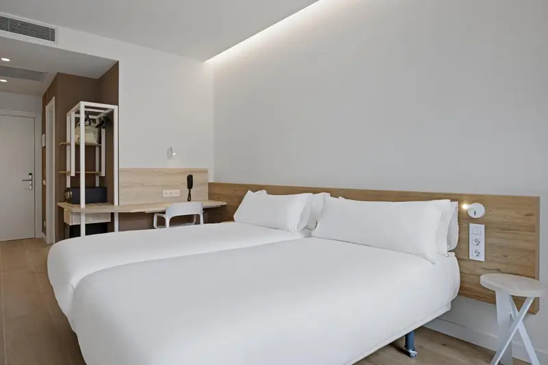 Une chambre lumineuse avec un grand lit blanc et un bureau.