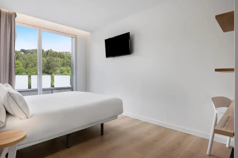 Chambre lumineuse avec un lit et une vue sur la végétation.