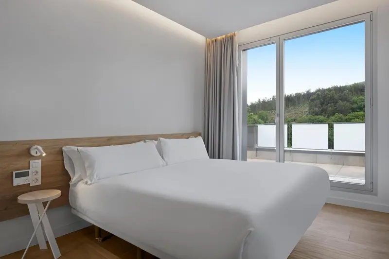 Une chambre lumineuse avec un grand lit et une vue sur la végétation.
