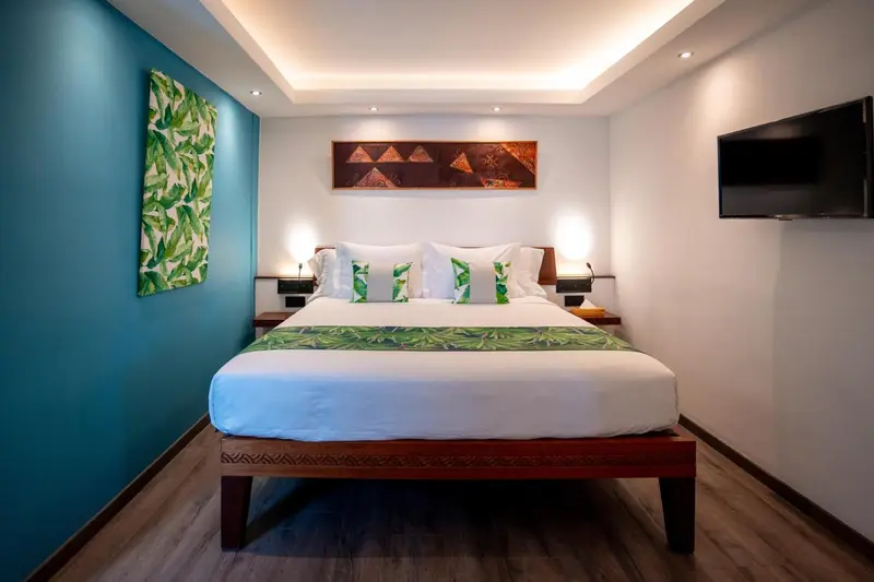 Une chambre lumineuse avec un grand lit recouvert d'une courtepointe blanche et de coussins verts.