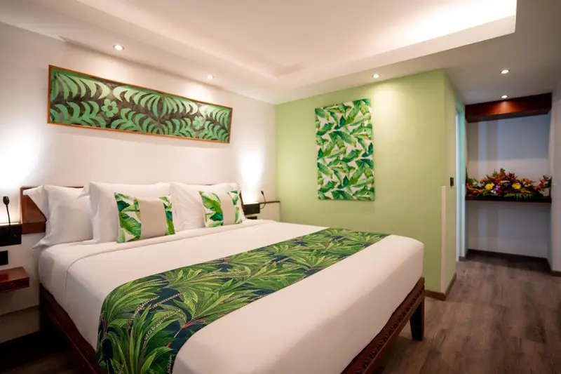 Une chambre lumineuse avec un grand lit recouvert d'une couette verte et blanche.