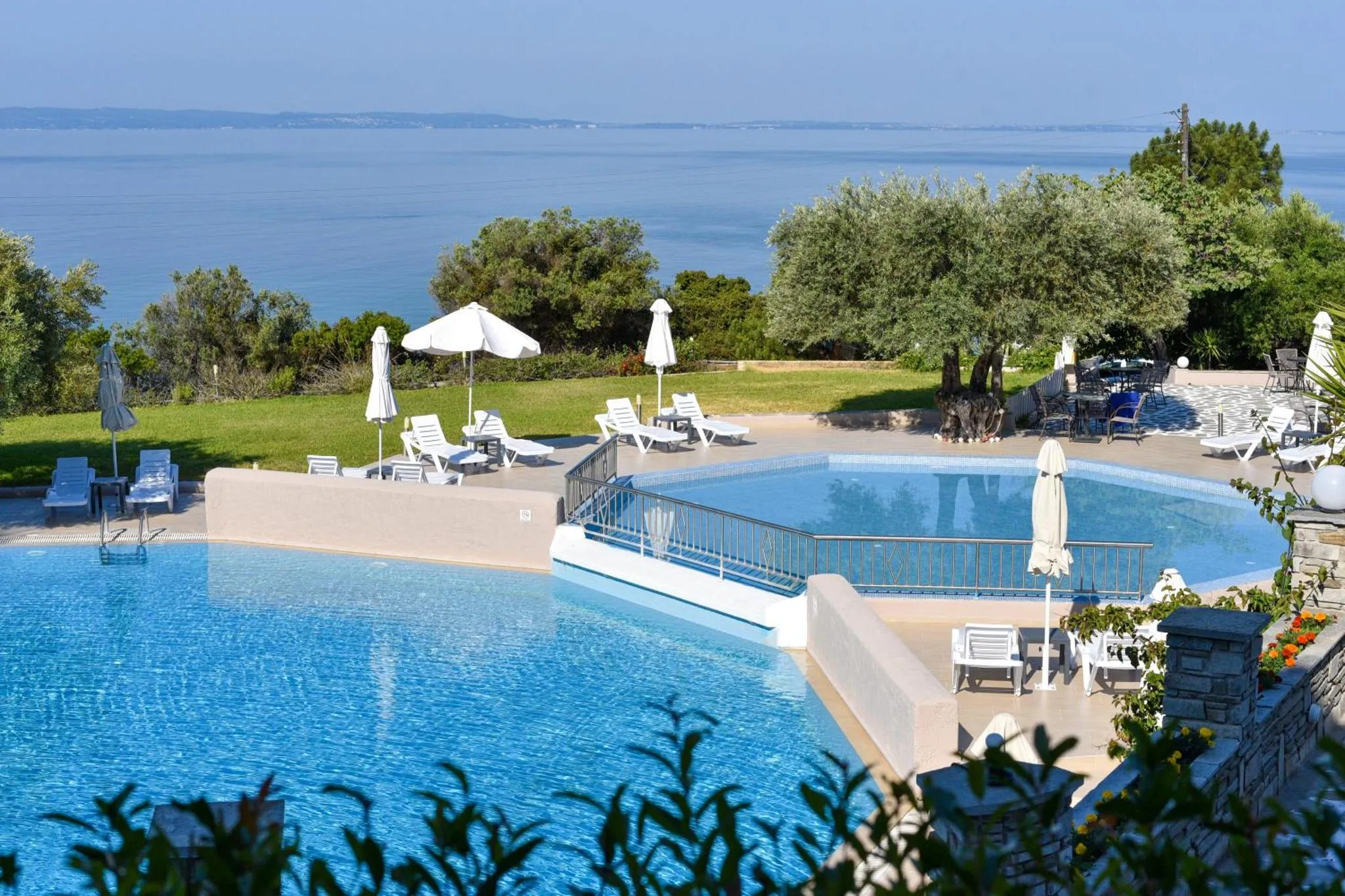 Piscine bleue avec transats et parasols, surplombant la mer.