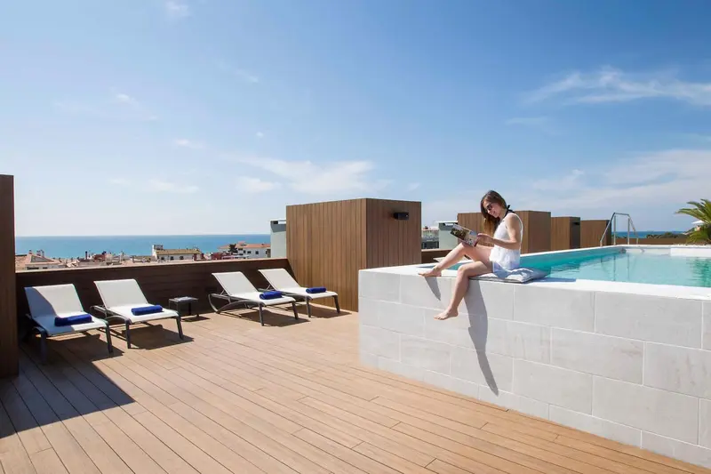Une femme est assise au bord d'une piscine sur une terrasse ensoleillée.