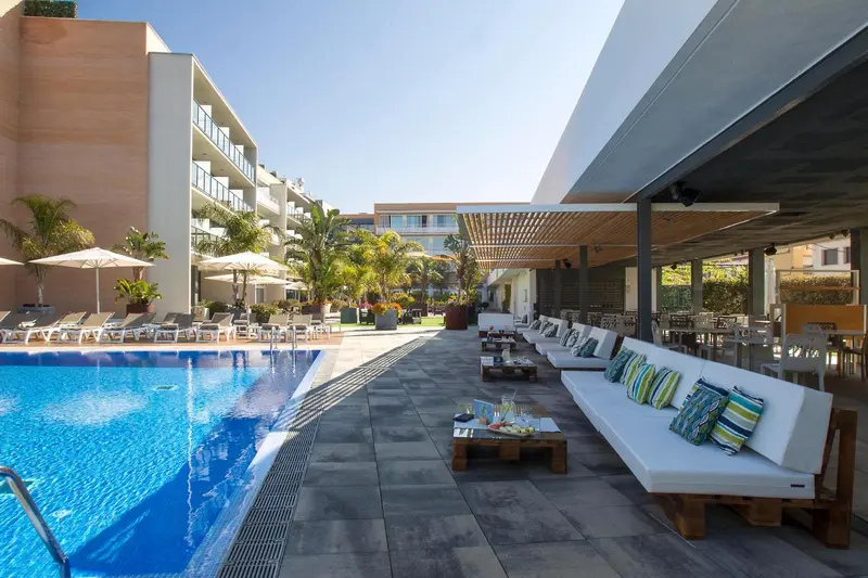 Espace de détente avec canapés blancs et coussins colorés près d'une piscine ensoleillée.