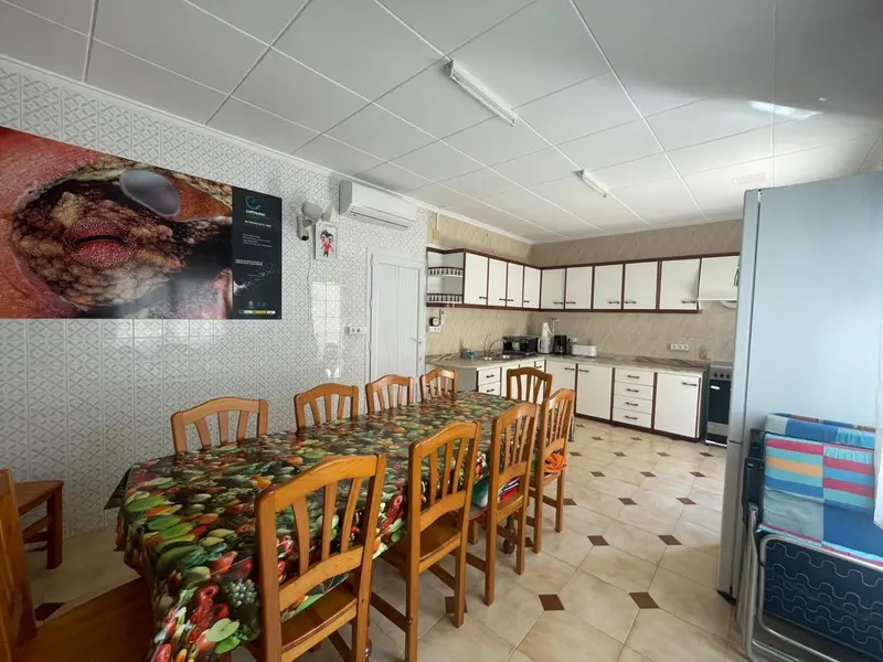 Une salle lumineuse avec une grande table à manger et des meubles de cuisine blancs.