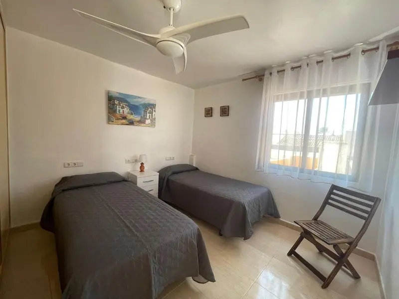 Une chambre lumineuse avec deux lits simples et un ventilateur au plafond.