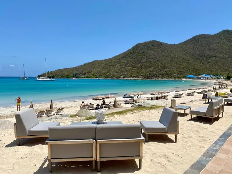 Mobilier de salon sur une terrasse de sable face à une plage ensoleillée.