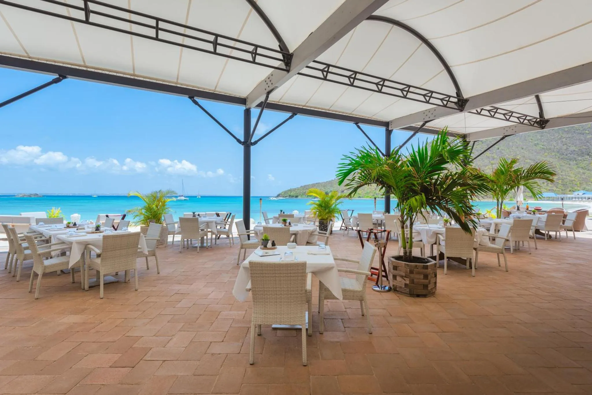 Terrasse ombragée avec tables et chaises donnant sur la mer turquoise.