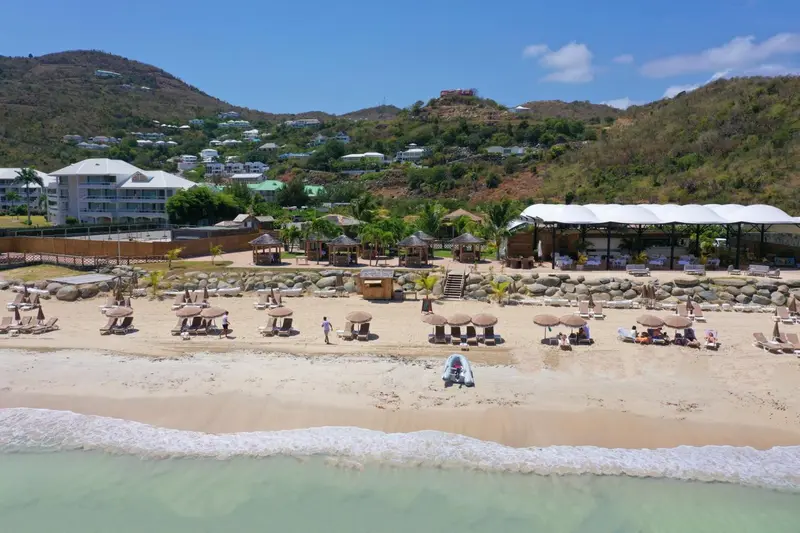 Vue aérienne d'une plage de sable fin bordée de transats et de parasols.