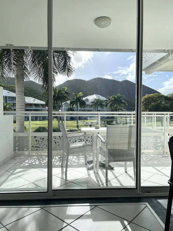 Terrasse avec mobilier blanc donnant sur un paysage tropical et des bâtiments.