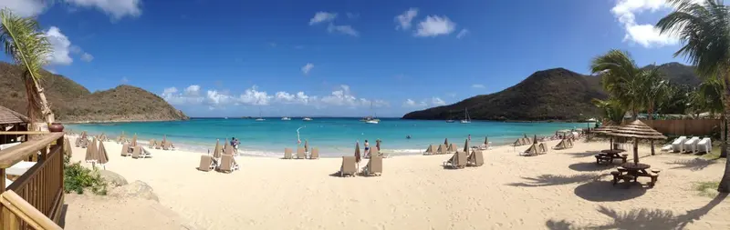 Plage de sable blanc bordée de transats et de parasols sous un ciel bleu.