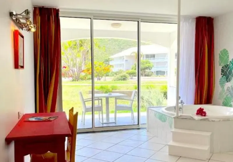 Une chambre lumineuse s'ouvre sur une terrasse avec vue sur un jardin tropical.