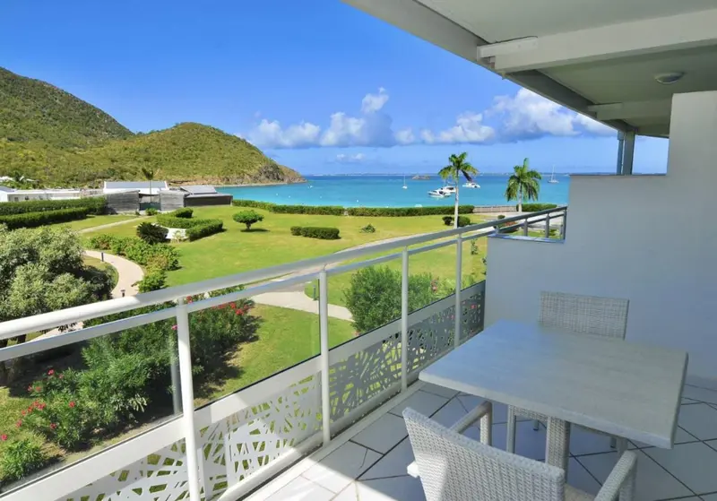 Vue d'une terrasse avec une table et des chaises donnant sur un paysage verdoyant et la mer.