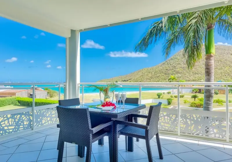 Table et chaises sur une terrasse avec vue sur la mer et la végétation.