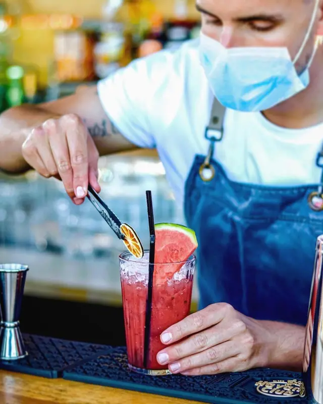 Un barman prépare une boisson colorée au comptoir.