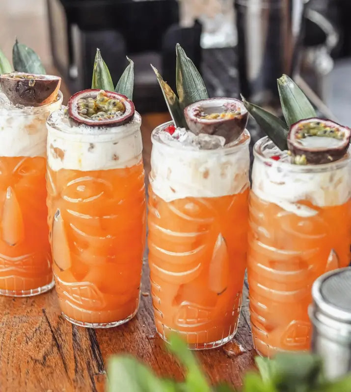 Quatre verres à cocktail exotiques ornés de fruits frais sont présentés sur une table en bois.
