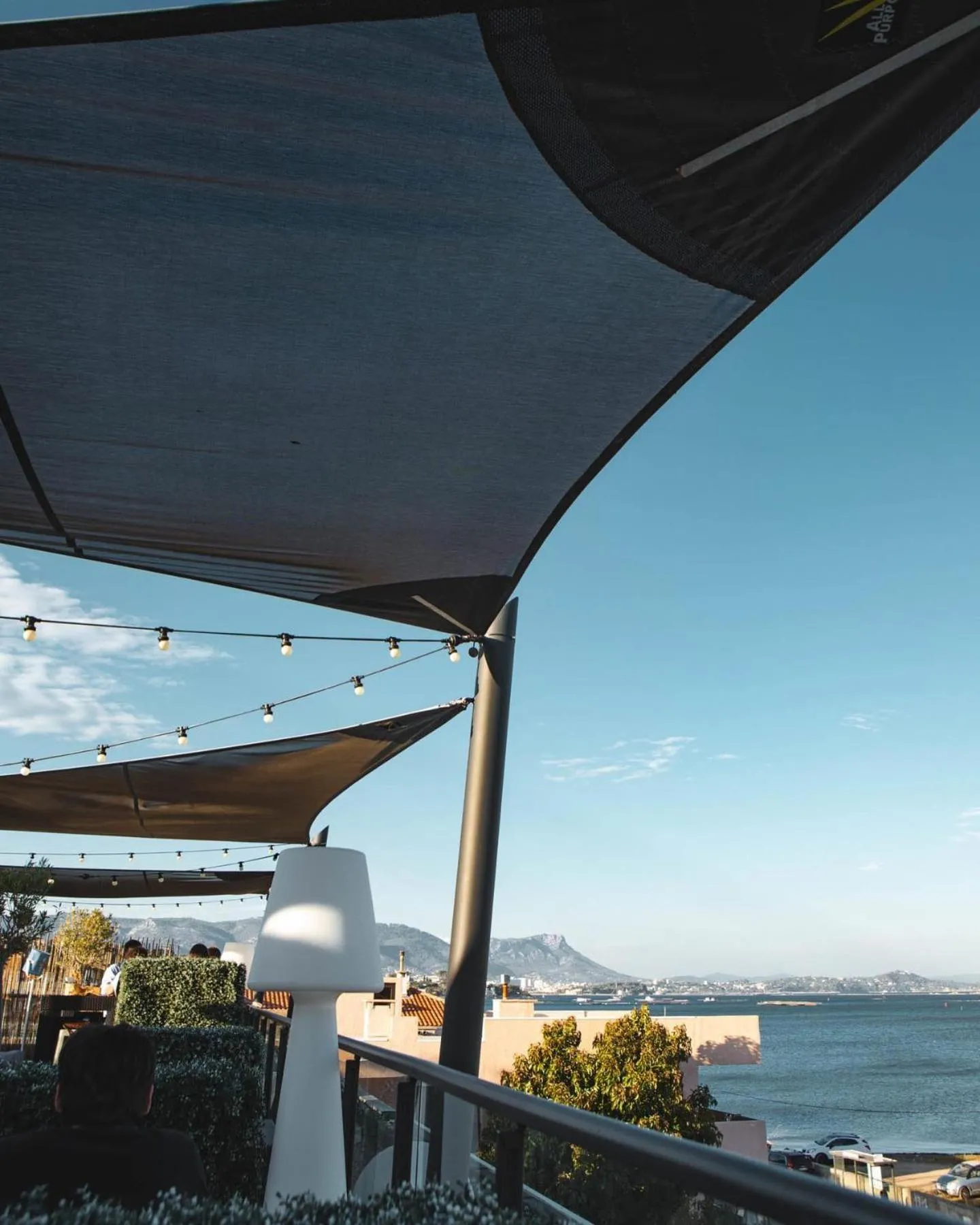 Terrasse ombragée avec vue sur la mer et les montagnes.